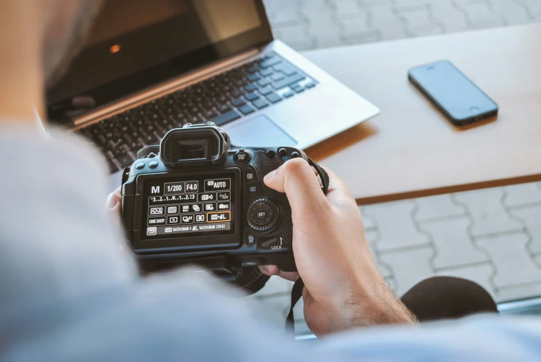 a man is holding a camera and using a laptop