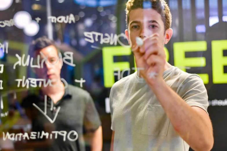 man pointing in front of glass with another man standing nearby