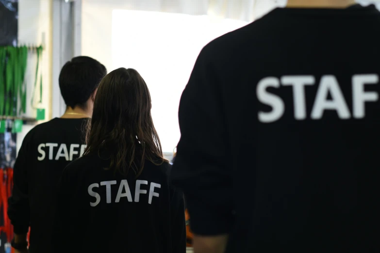 a man and a woman with long hair are standing in a room that has staff shirts on