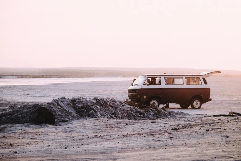 a van with a surfboard mounted to the top driving down a sandy beach