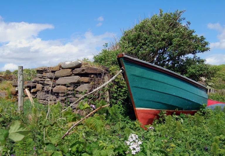 a boat is sitting in weeds beside a rock pile