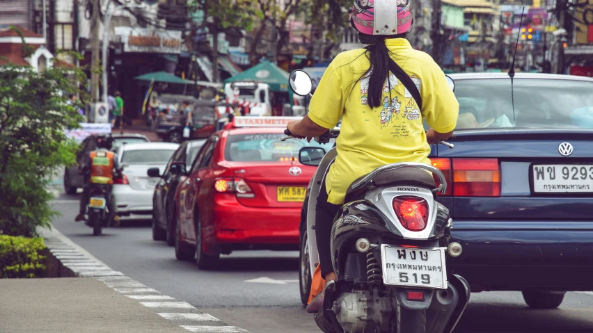 a woman in yellow shirt riding on motorcycle next to cars