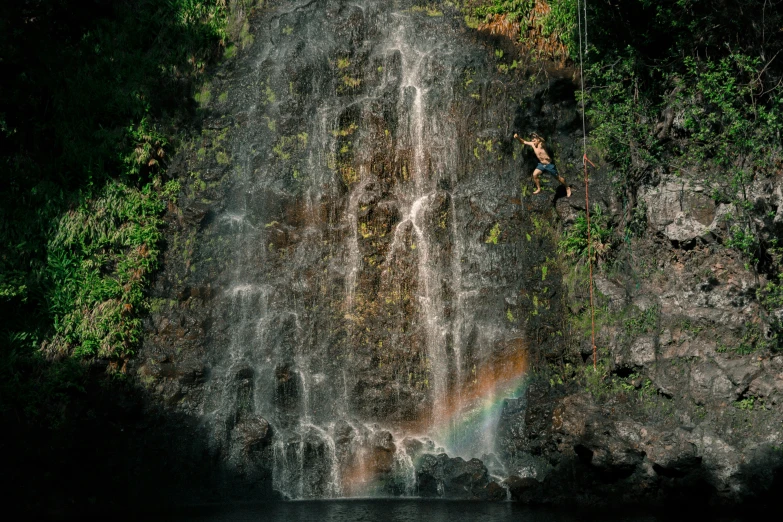the water was almost clear and there is a man leaping over the waterfall
