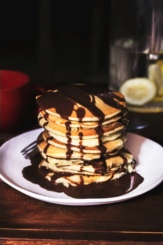 a stack of pancakes with syrup, chocolate sauce and a red mug