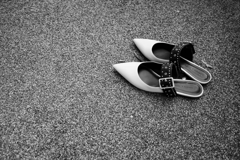 pair of shoes sitting on pavement with one wearing an embellished strap