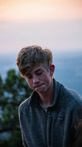 a boy is looking at the camera while holding his nose with mountains in the distance