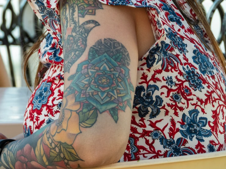 tattooed woman in red and white shirt sitting at table with cup of coffee