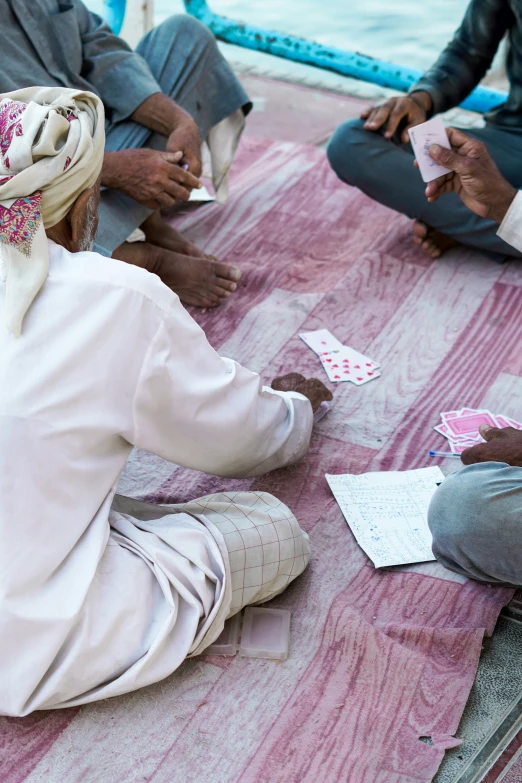 a group of men sitting on the ground playing cards