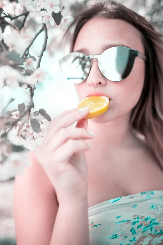 a woman wearing sunglasses holding a slice of fruit