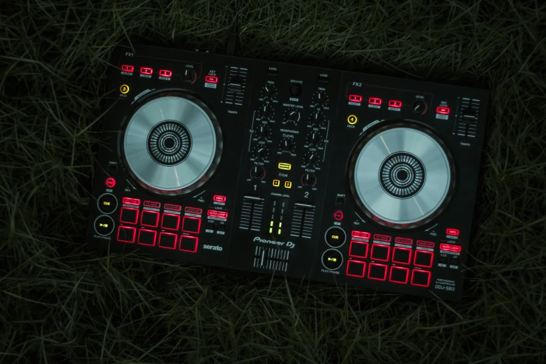 a dj controller laying on grass with its lights on