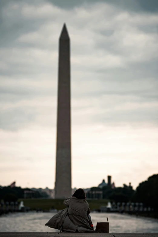 a person sitting on a ledge near a obelisk