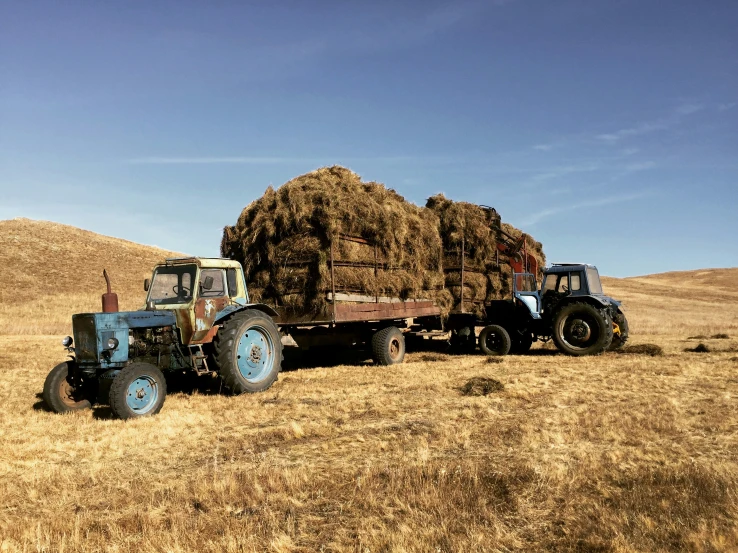 a blue tractor pulling a trailer of hay on a field