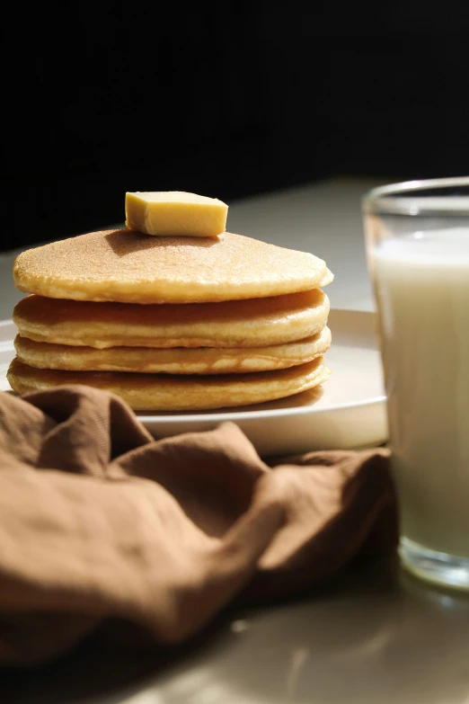 a stack of pancakes next to a glass of milk