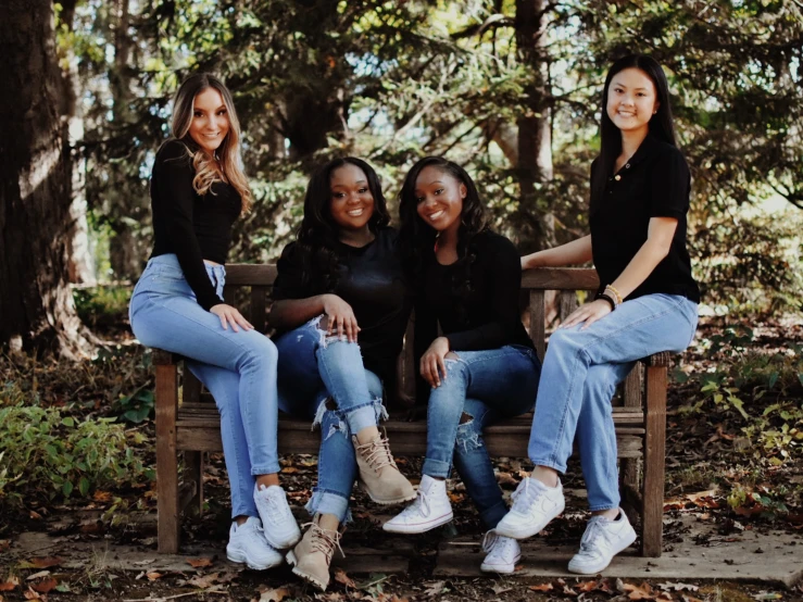 three smiling women sitting on a bench by some trees