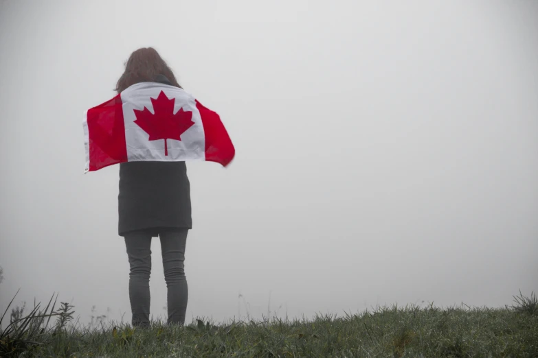 someone holding a canadian flag and standing on top of a hill