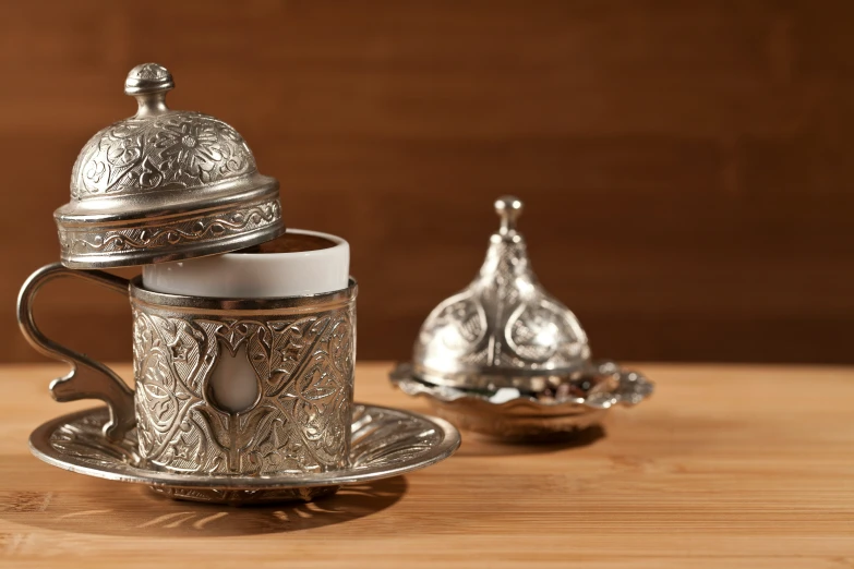 a silver cup and saucer sitting on a wooden table