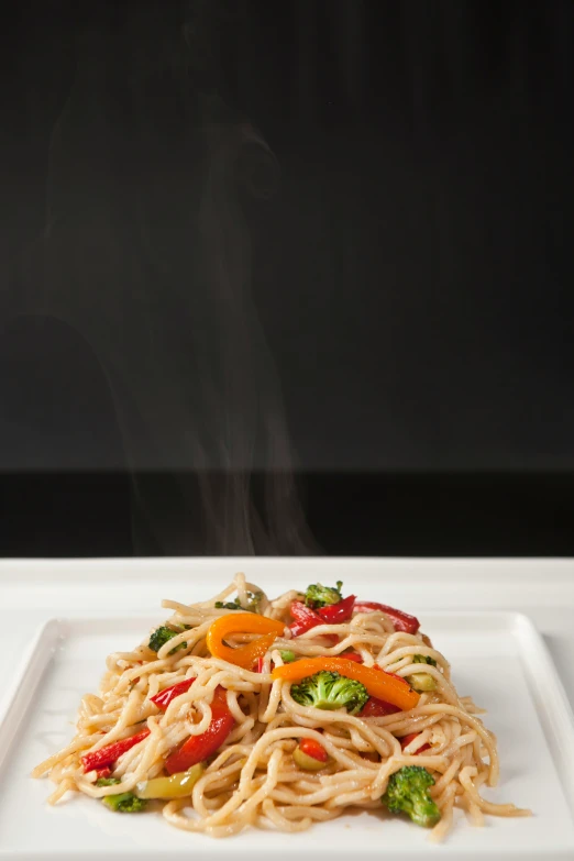 a plate of noodles and vegetables is shown with steam rising from the top