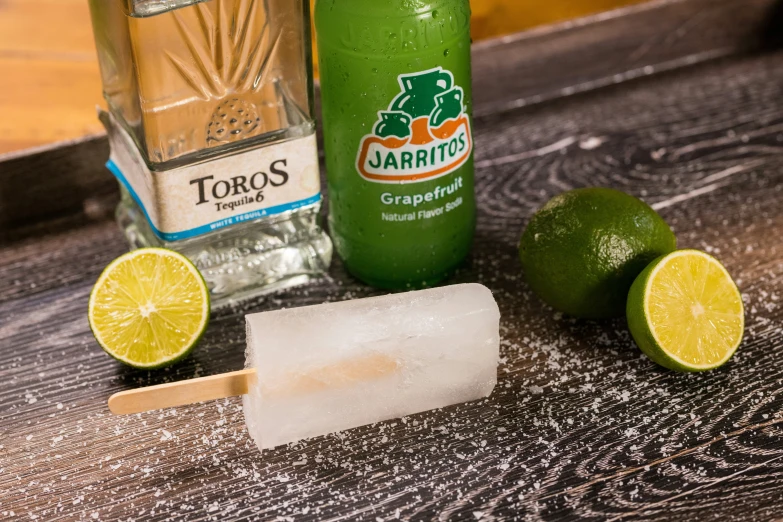 margarita pops with two lime wedges, lime wedges, and a bottle of tequila