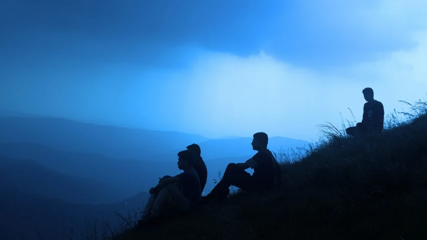 three people sitting on a hill under a dark sky