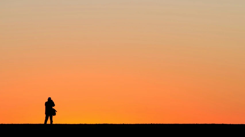 a lone man standing at the top of a hill as the sun sets