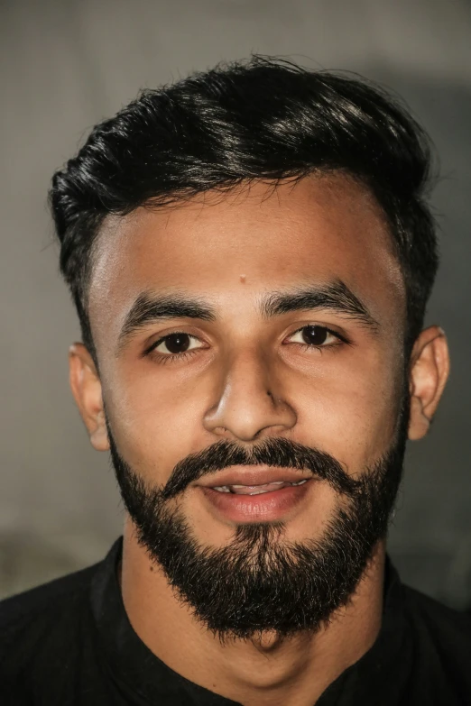 a man with black shirt and beard in front of gray background