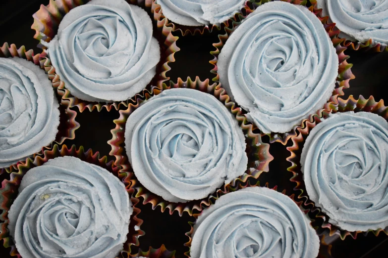 several cupcakes with white frosting on a dark surface