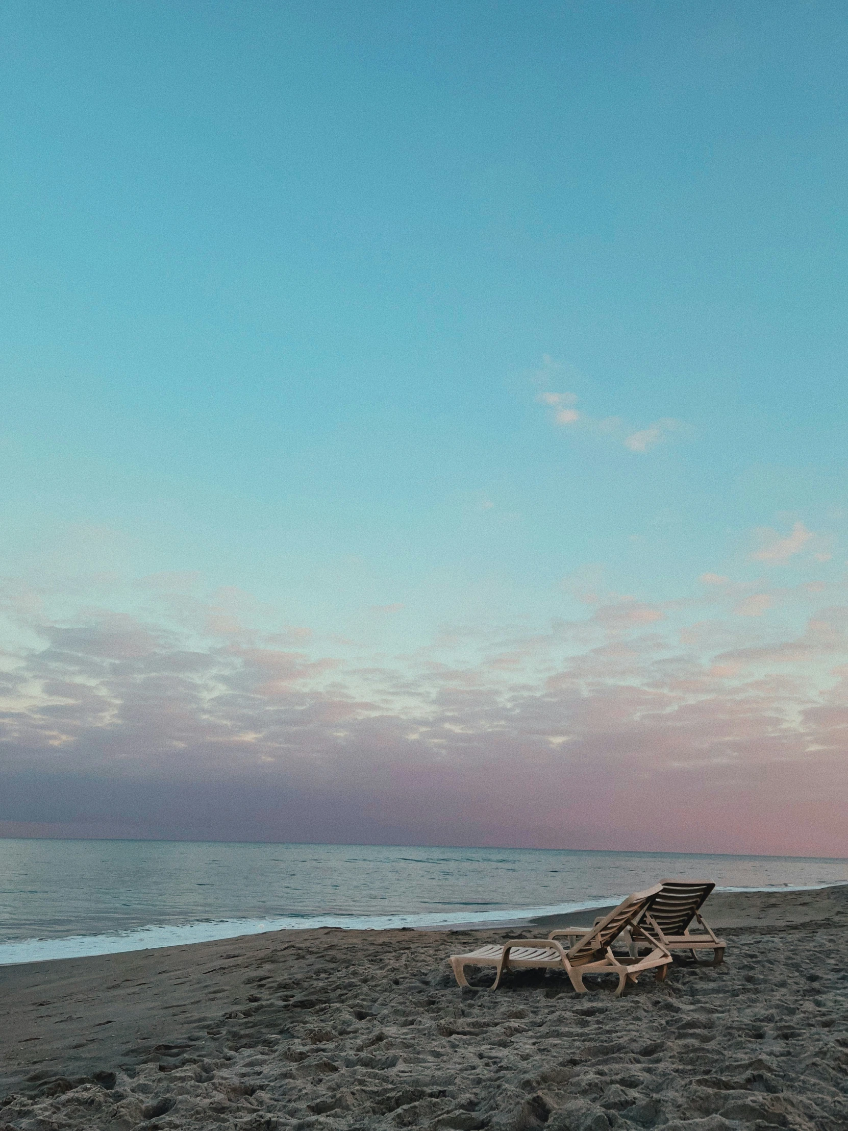 two empty beach chairs sit next to a sandy beach