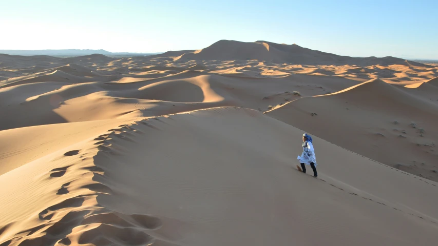 a woman standing on top of a very large sand dune