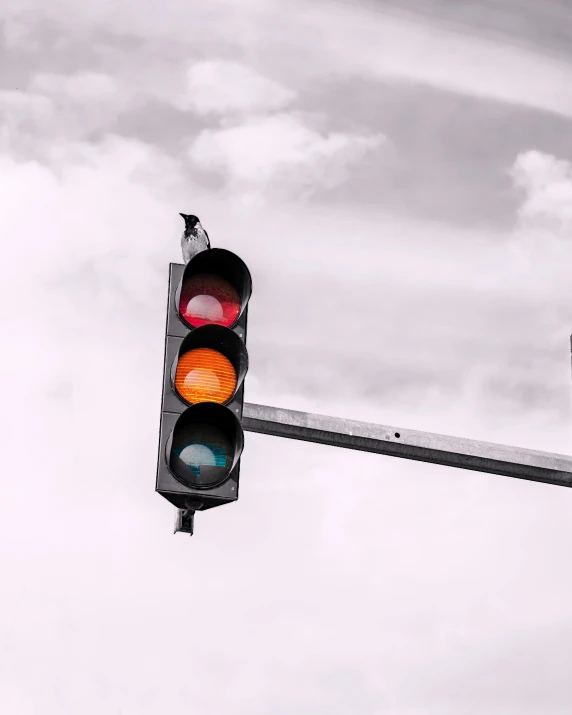 a red traffic light sitting below a cloudy sky