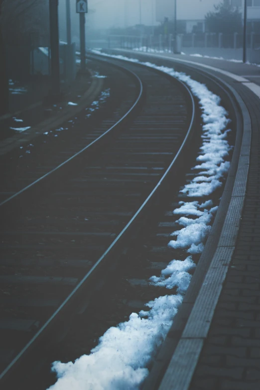 an empty train track with clouds of snow on the tracks