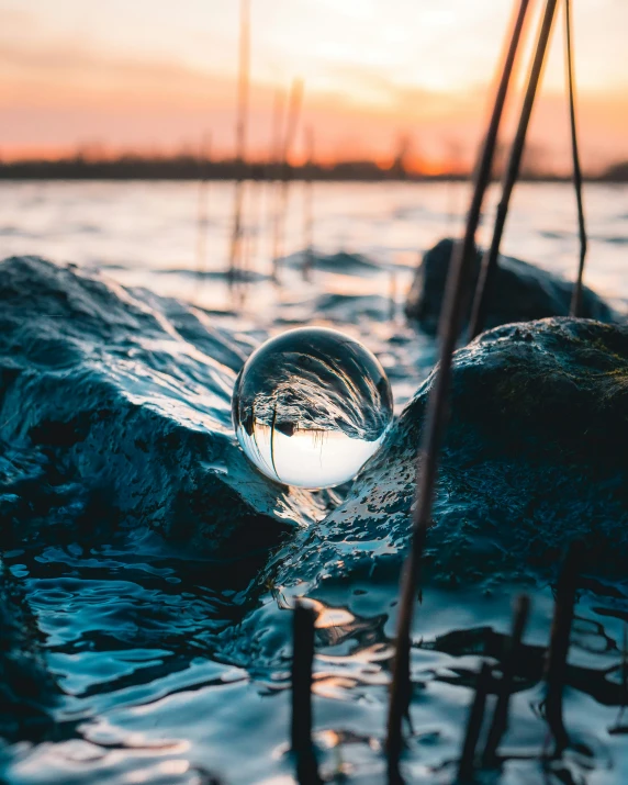 a sphere shaped object floating in the water near a rock