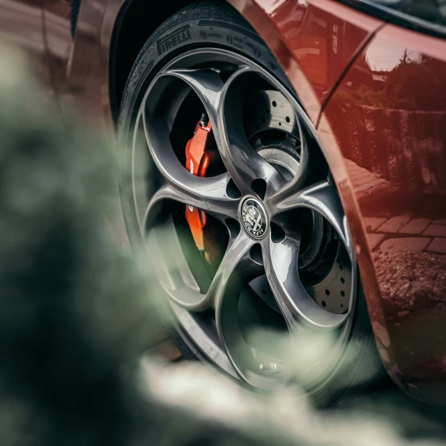 a red car with grey wheels and some leaves