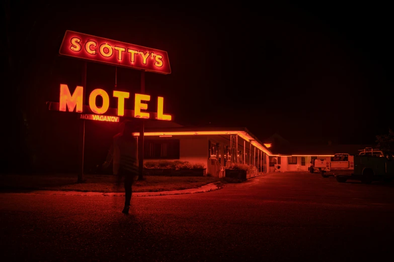 a motel sign lit up at night with someone walking past