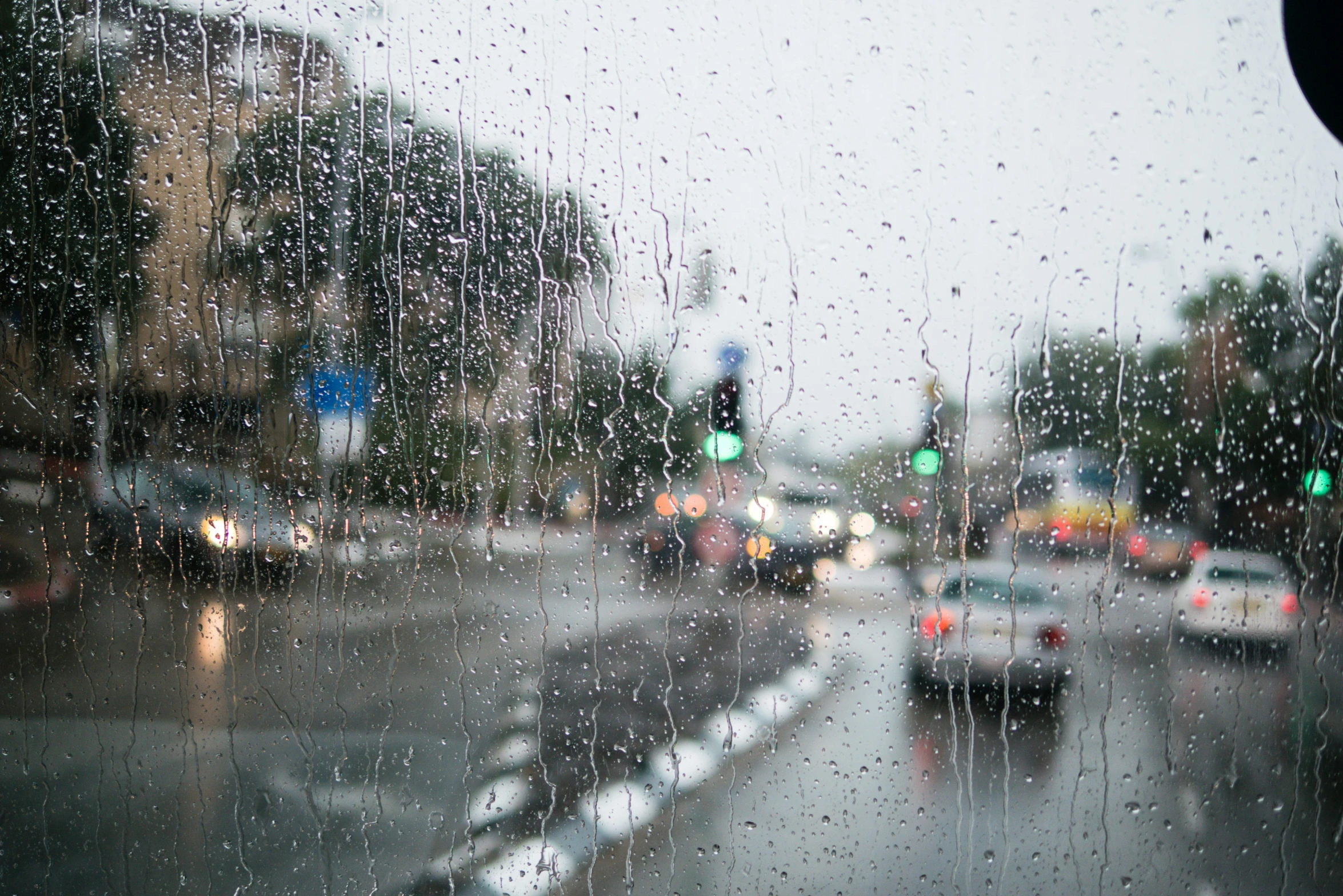 rain is coming down from a traffic light as cars drive through the city