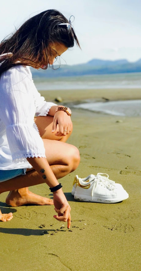 a woman bending down on a beach next to a shoe