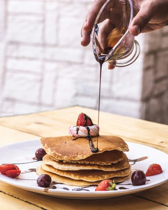 a person pours syrup on a stack of pancakes