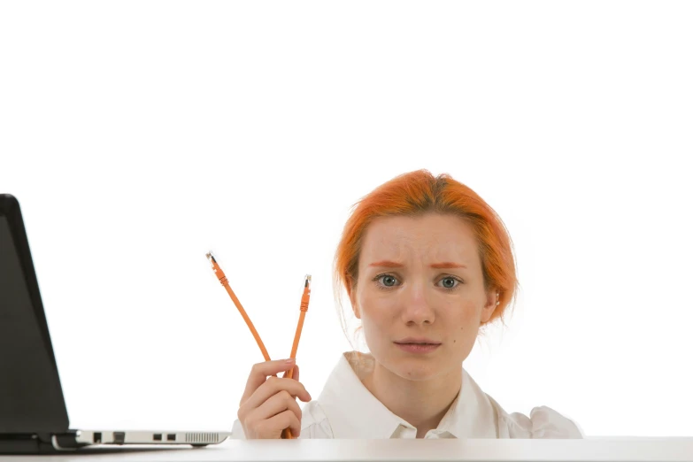 a redhead girl holds two pencils while at a computer