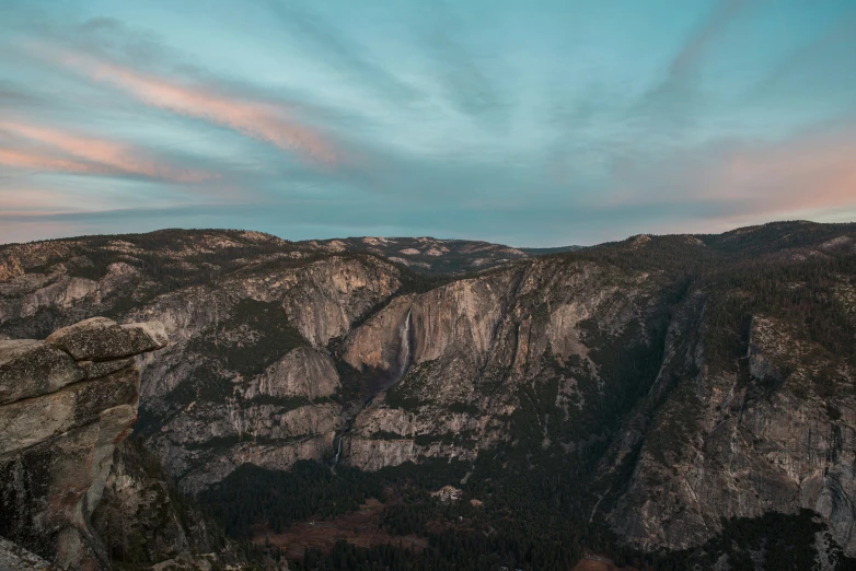 a mountain cliff with mountains in the distance under a blue sky