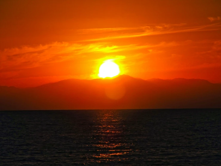 the sun is setting behind a mountain range in the ocean