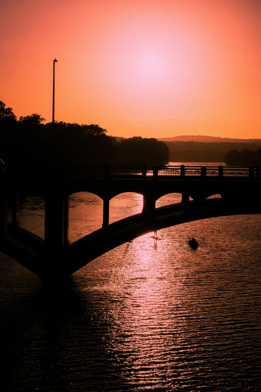 sunset over the water with some bridges and a boat