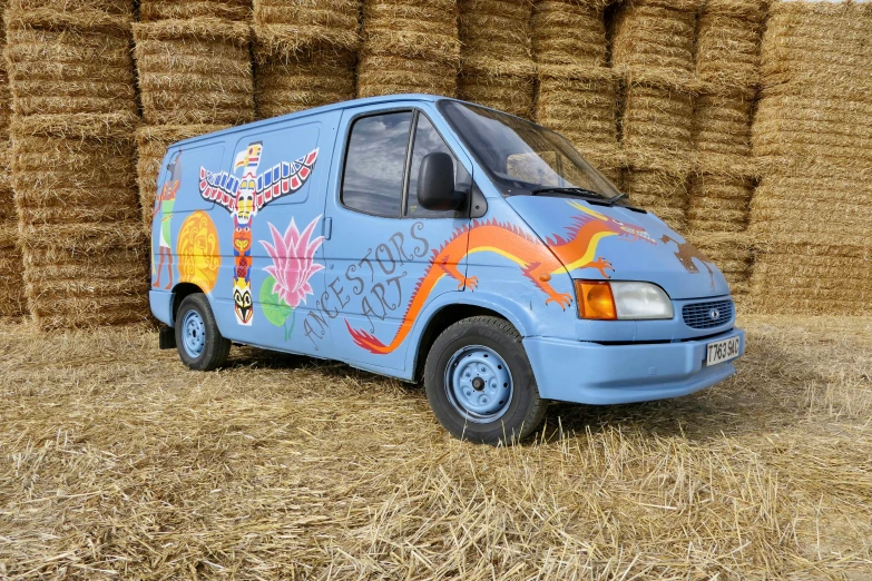 a van with decorations painted on the front is parked in front of a stack of hay bales