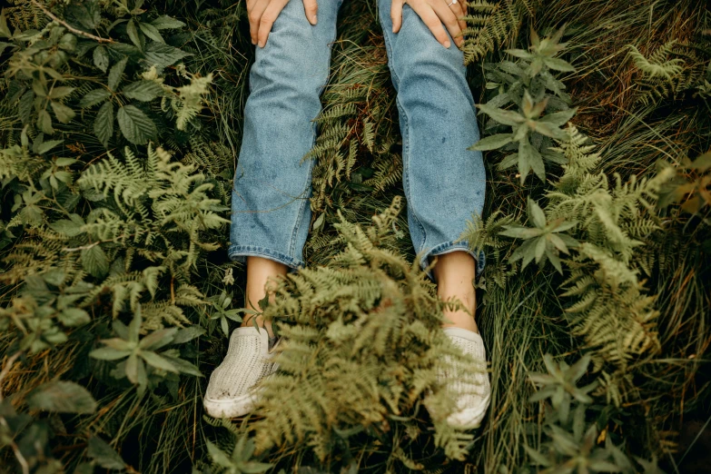 a woman sitting on the ground, her hands tucked under her knees and her shoes out