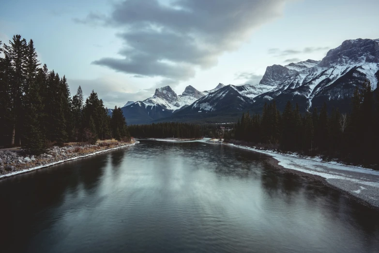 a stream is surrounded by snow capped mountains