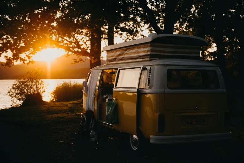 the sun is setting behind a van by the water