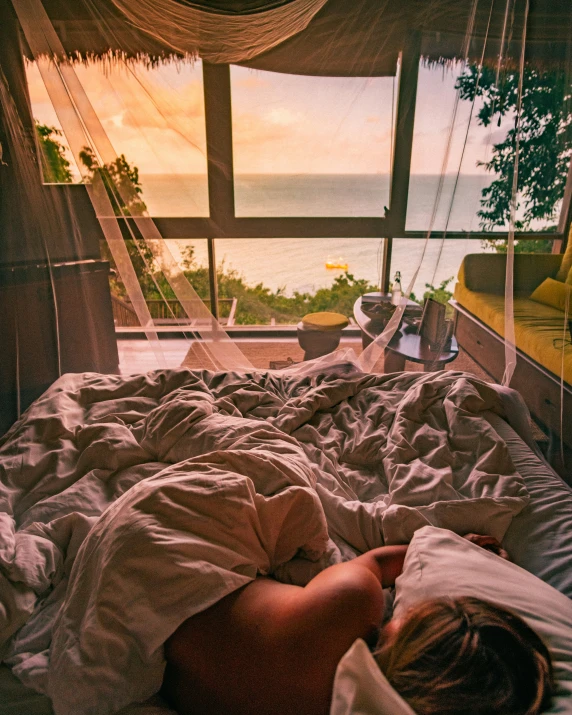 a person laying in bed with an ocean view out the window