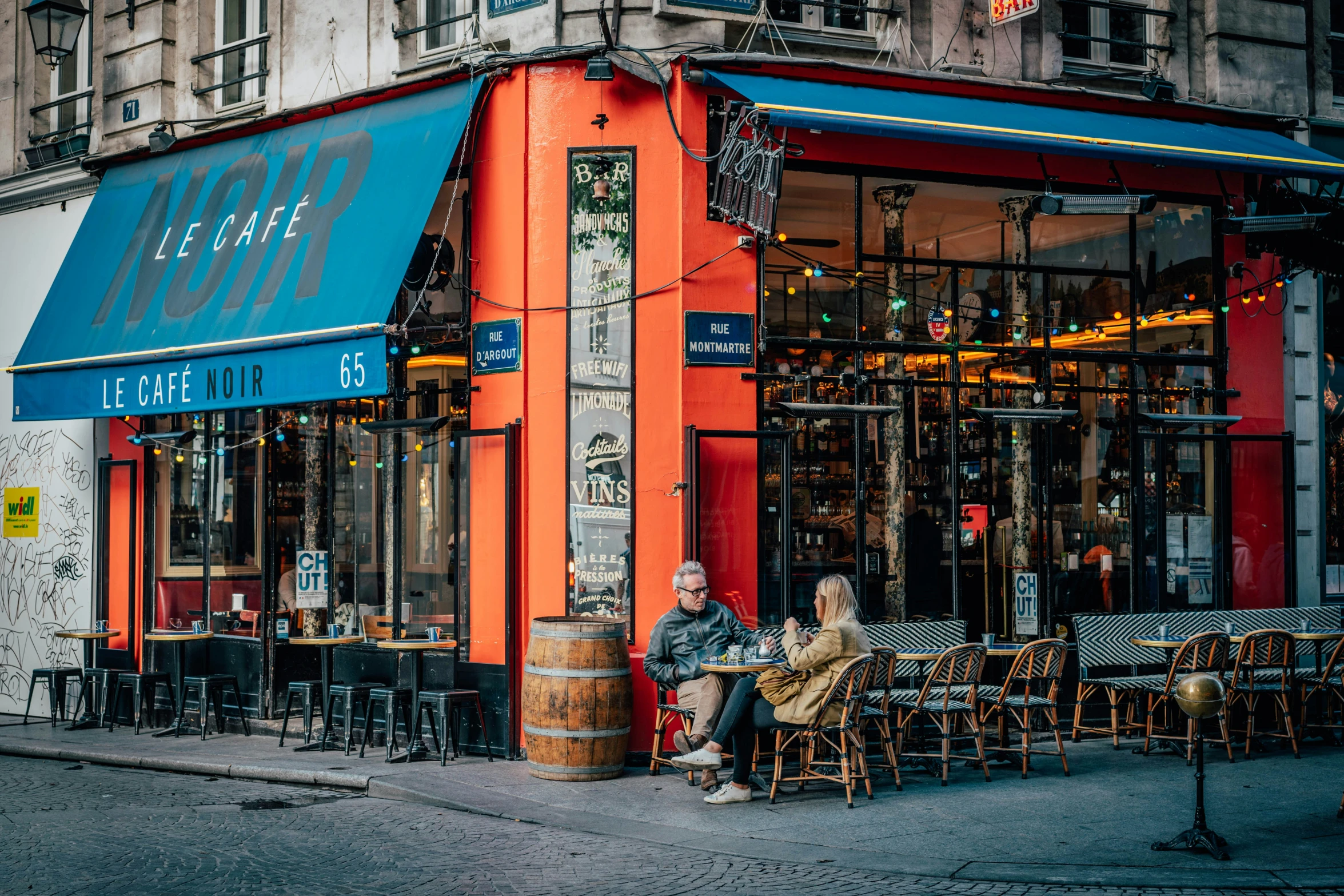 two people sitting outside an orange restaurant in paris