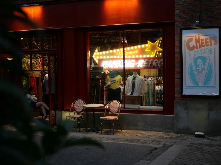 a storefront with people walking by it and there is a table and chairs outside