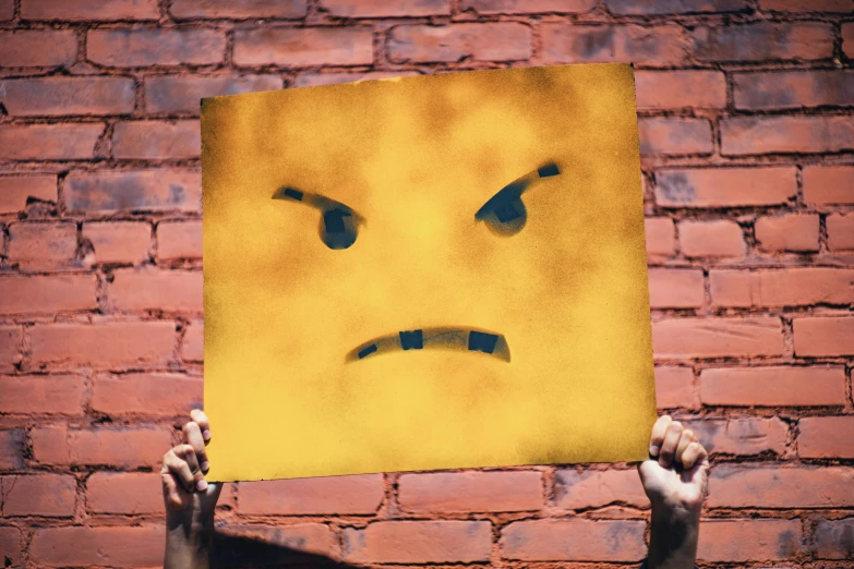 someone holds up a piece of yellow paper with a crying face painted on it