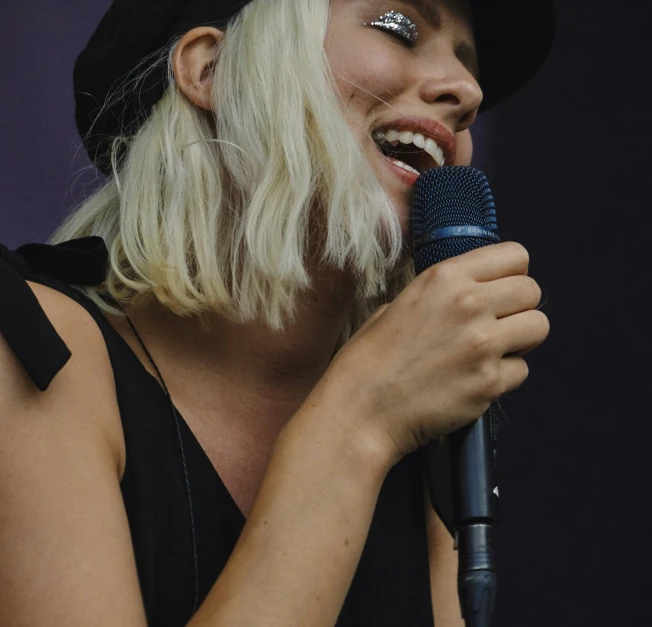 a woman with blonde hair and makeup singing into a microphone