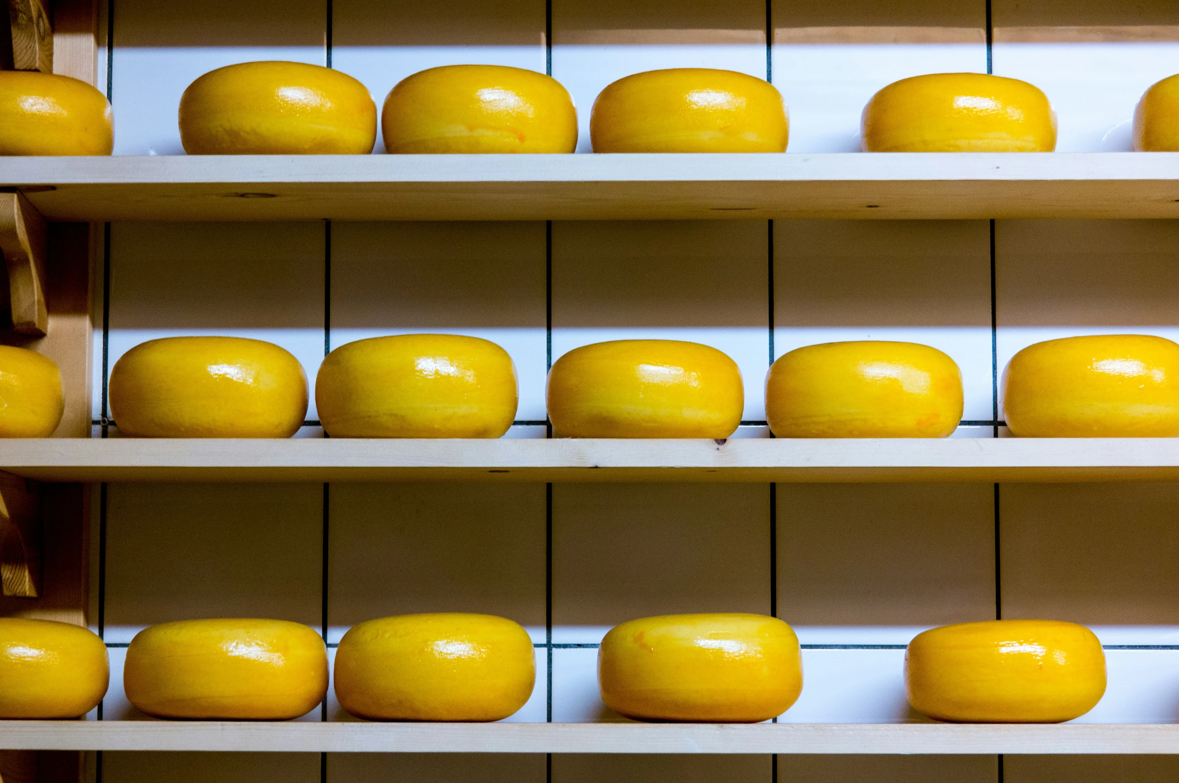 shelves filled with various yellow cheeses on a white shelf